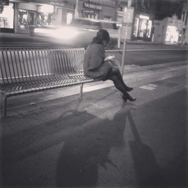 Day 19 - Woman sits hunched in the cold evening air waiting for a tram. She is alone.