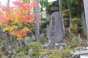 Autumn. Large stone with Japanese writing carved into it on right. Tree with yellow and red foliage on the left. Japan.