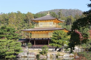 large three tiered Japanese pagoda style building. upper two floors are covered in cold. Forest and mountain in background.