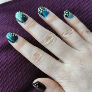A right hand displaying black, teal and yellow patterened nail polish