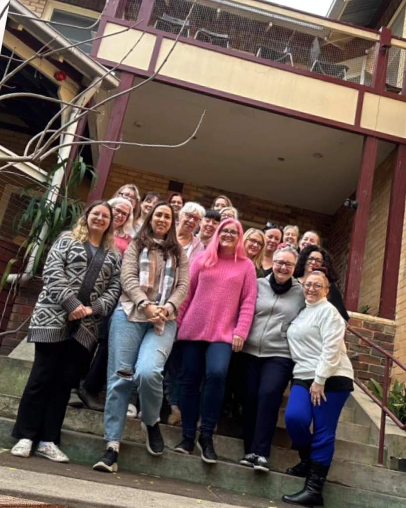 A photo of eighteen women standing in a group on steps in front of a building.