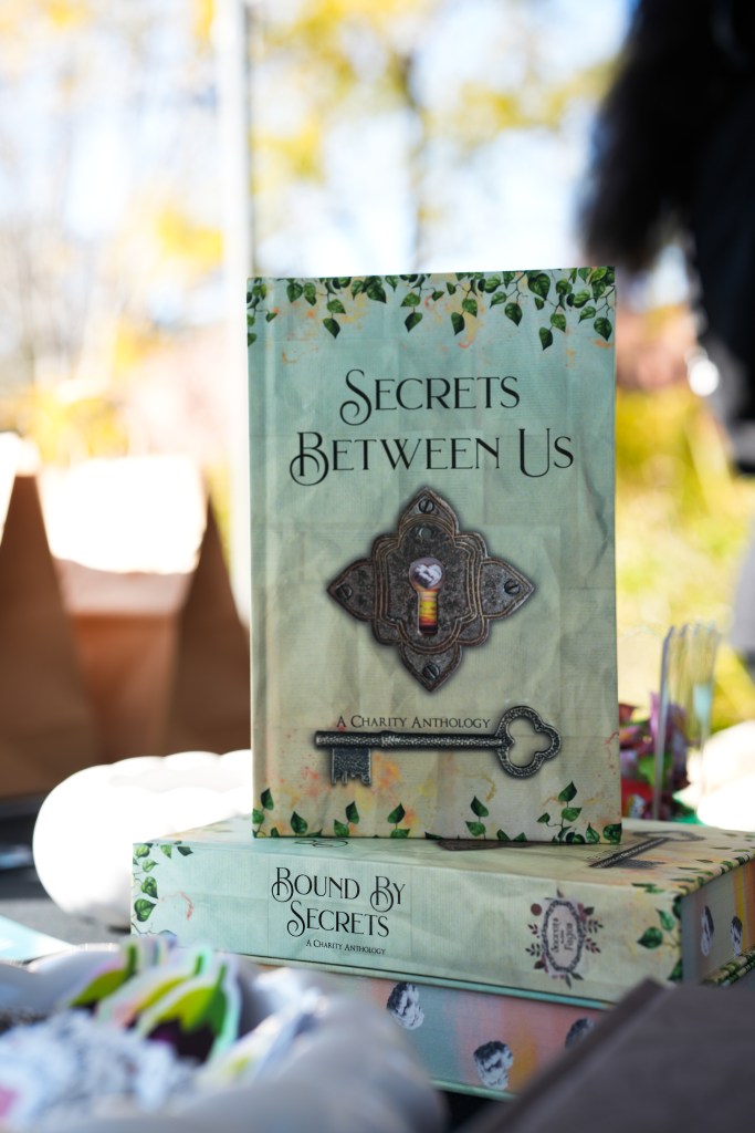 A book is displayed, it is mostly green, and shows a key and ornate lock. The cover reads 'Secrets Between Us'